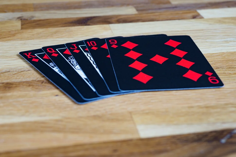 Five black playing cards showing nine through king of diamonds, fanned on a wooden table.