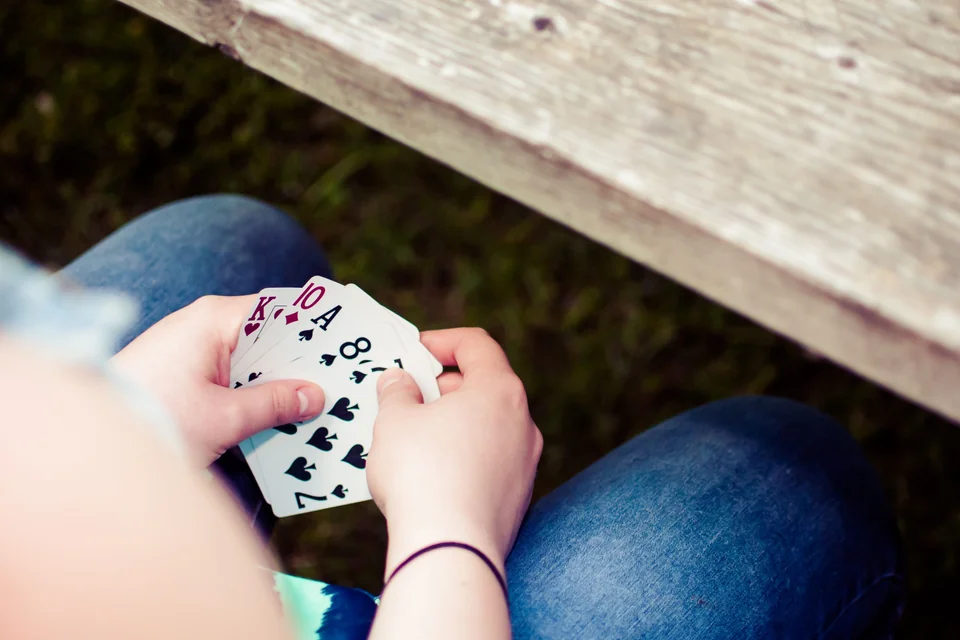 Hands holding a fan of playing cards outdoors.